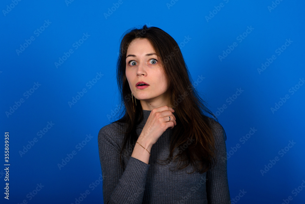Photo of smiling, cheerful young female in grey dress on blue background Photo of smiling, cheerful young female in grey dress on blue background