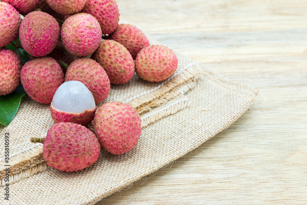Pile of fresh lychee sweet fruit and peeled showing white fleshon on hemp sacks and wood background with copy space, Tropical fruits in thailand.
