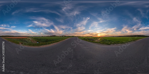 Full spherical seamless panorama 360 degrees angle view on old no traffic asphalt road among fields in evening  before sunset with cloudy sky in equirectangular projection  VR AR content