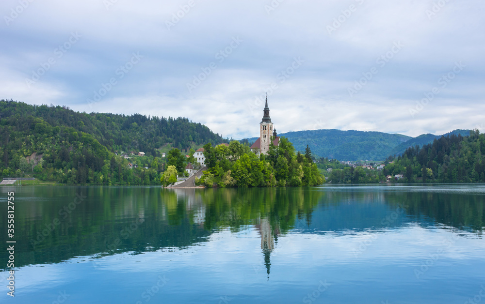 Beautiful morning at Lake Bled and Julian Alps in the background. The lake island and charming little church dedicated to the Assumption of Mary are famous tourist attraction in Slovenia