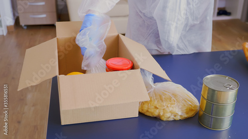 Close up of volunteer packing food in box for delivery wearing protective suit during gloabal covid-19 pandemic photo