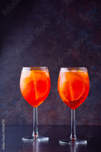 Aperol spritz cocktail in glass on dark background. Two glasses of aperol spritz with sliced orange. Summer cocktail in glass. Copy space