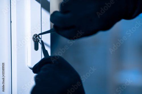 Robber in black balaclava cracking door with metal picklock