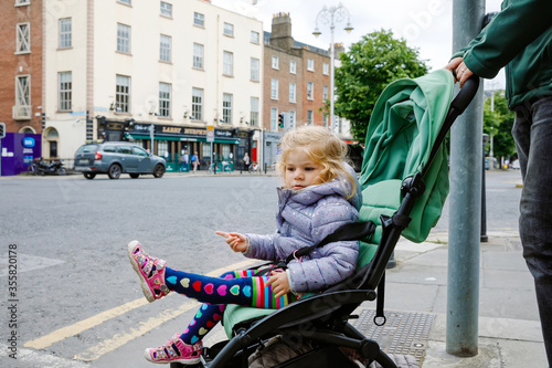 Photography Cute little toddler girl sitting in baby stroller while walking with dad on the streets of big city