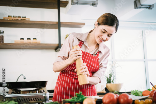 Asian female chef dressed in an apron cooking in the kitchen sprinkling Crushed pepper on raw salmon To prepare food on the modern kitchen counter