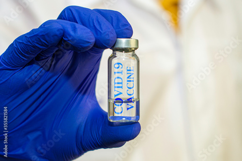 vial with the vaccine in the hands of a doctor in blue protective surgical gloves inscription on the vial COVID19 vaccine doctor in the background in blur