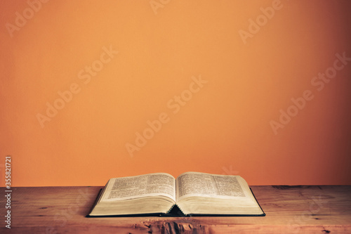 Open Holy Bible on a old wooden table. Beautiful orange wall background..