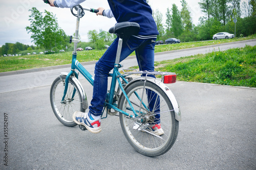 Bicycle and legs of a child starting riding it in jeans and sneakers. Skewed horizon.