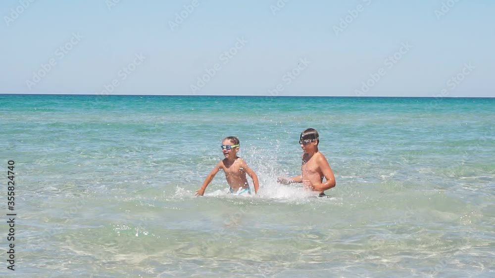 Children, boys against the background of the endless azure, turquoise sea and blue sky play splashing in the water, a Sunny summer day. Two brothers have fun playing in the sea making splashes and Children, boys against the background of the endless azure, turquoise sea and blue sky play splashing in the water, a Sunny summer day. Two brothers have fun playing in the sea making splashes and