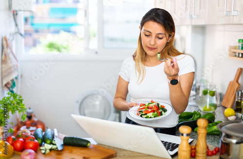 Peruvian housewoman eating salad and watching movie on laptop photo