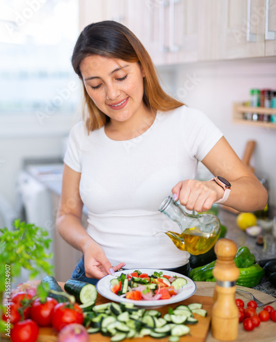 Young peruvian housewoman add oil to salad vegetable