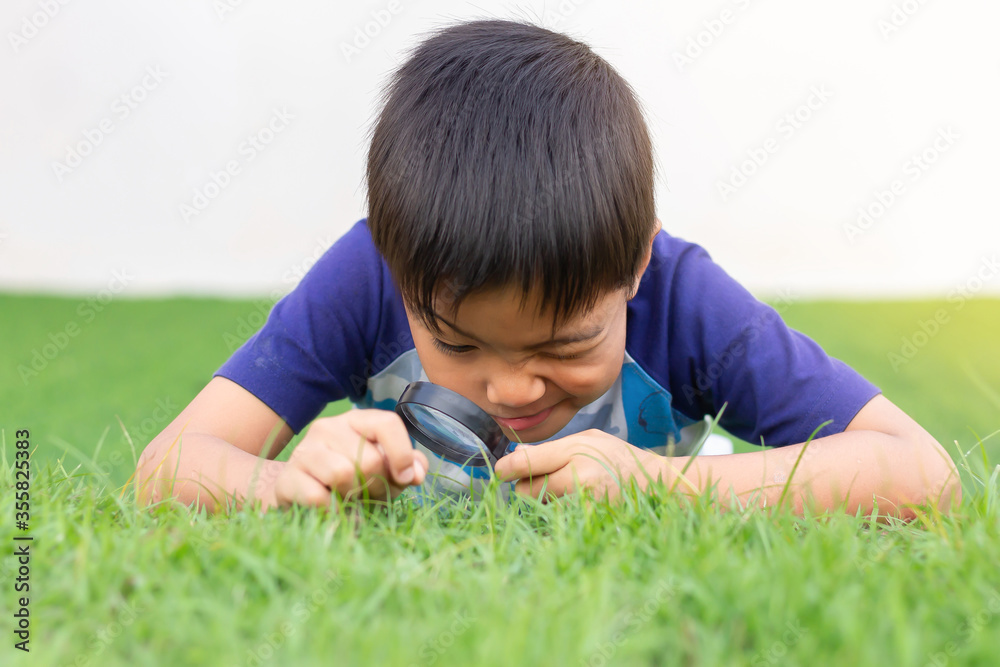 Portrait of happy Asian child boy holding and looking with magnifying glass on the flower tree and green grass field floor. Adventure, explorer and learning kid. Childhood 5-6 years old. Portrait of happy Asian child boy holding and looking with magnifying glass on the flower tree and green grass field floor. Adventure, explorer and learning kid. Childhood 5-6 years old.