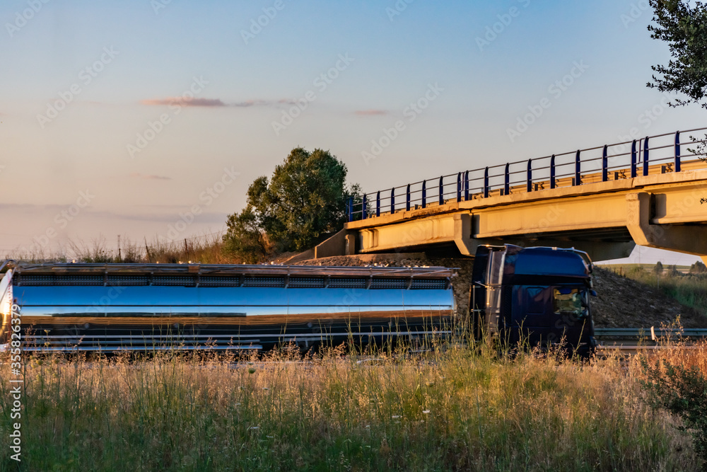 Steel tanker truck driving on the highway with a sunset sky Steel tanker truck driving on the highway with a sunset sky