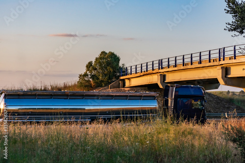 Steel tanker truck driving on the highway with a sunset sky