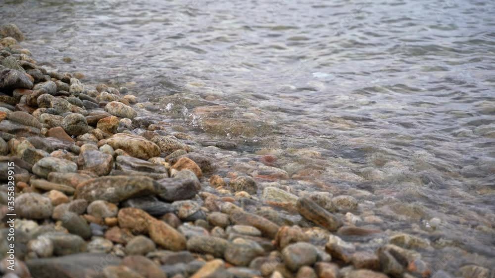 Calm tranquil waves lapping on a pebble beach, shore in day time. Wet stones on Lake Baikal. Calm tranquil waves lapping on a pebble beach, shore in day time. Wet stones on Lake Baikal.