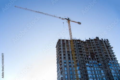 Tower crane working at construction site on blue sky background with white clouds. Construction process of the new residential buildings. Installing double glazed windows