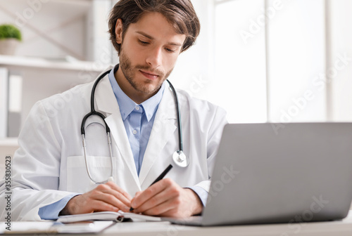 Doctor watching webinar on laptop and taking notes
