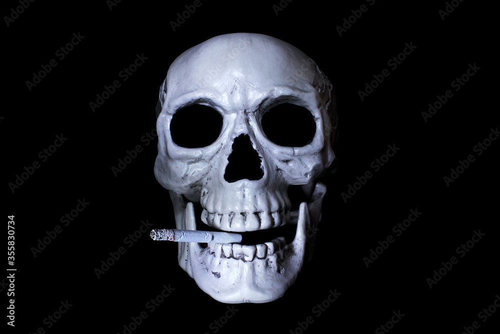 Human skull with a smoldering cigarette in the mouth. Isolated on black. Danger of smoking concept.