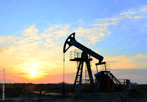 Oil drilling derricks at desert oilfield for fossil fuels output and crude oil production from the ground. Oil drill rig and pump jack on the background, sunset. Belarus, Rechitsa region