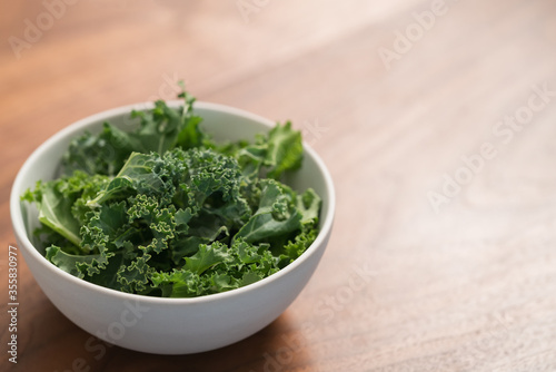 kale salad leaves in white bowl on walnut table with copy space