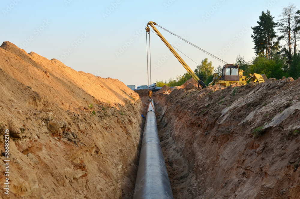 Natural gas pipeline construction work. A dug trench in the ground for the installation and installation of industrial gas and oil pipes. Crawler crane bulldozer with side boom or pipelayer Natural gas pipeline construction work. A dug trench in the ground for the installation and installation of industrial gas and oil pipes. Crawler crane bulldozer with side boom or pipelayer