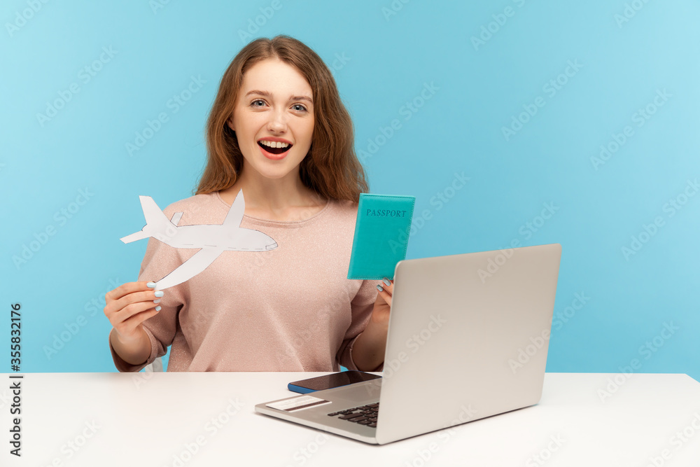 Amazed woman, travel agent holding passport and paper airplane, looking at camera with excitement and surprise, advertising hot tours with airline transportation. indoor studio shot, blue background Amazed woman, travel agent holding passport and paper airplane, looking at camera with excitement and surprise, advertising hot tours with airline transportation. indoor studio shot, blue background