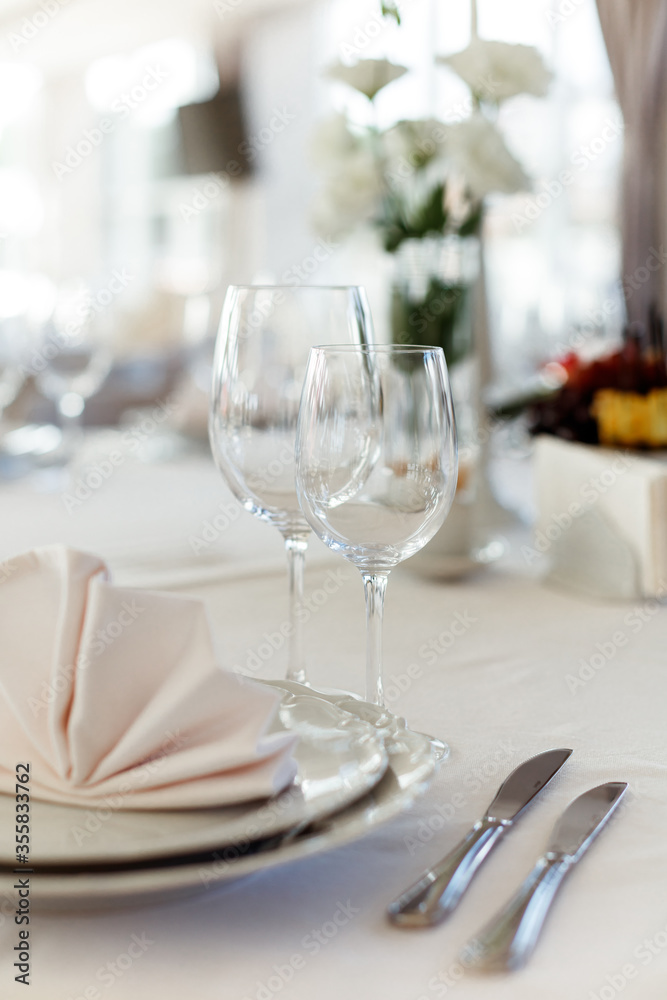Plates, glasses, cutlery and flower arrangement on a white round table.