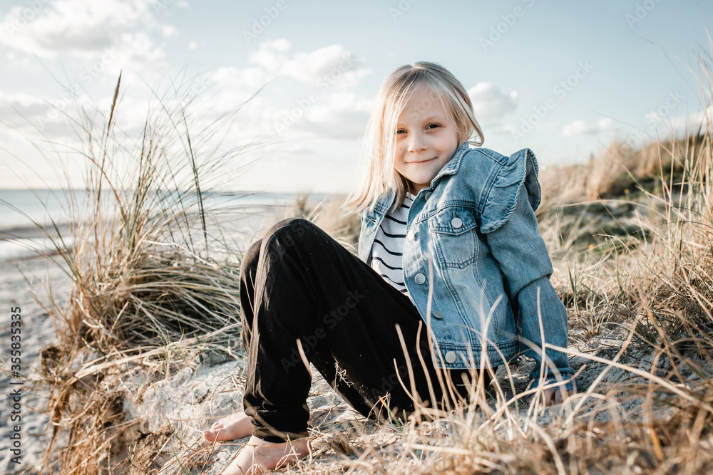 Young girl at the beach, sitting on a sand dune looking at the camera Young girl at the beach, sitting on a sand dune looking at the camera