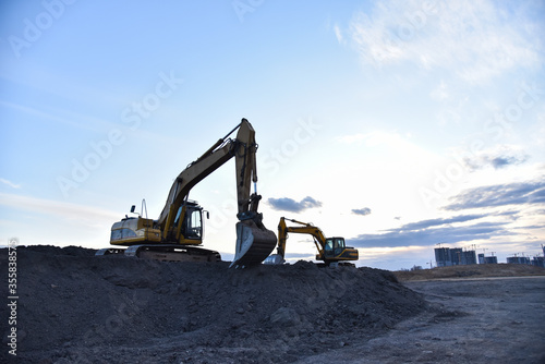 Excavators work at constrruction site on sunset background. Backhoe digs gravel and old concrete. Recycling old asphalt at a landfill for the disposal of construction waste. Construction machinery