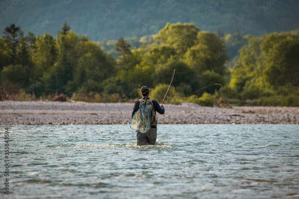 A fly fisherman casts his line while standing in the middle of a river A fly fisherman casts his line while standing in the middle of a river