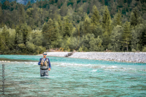 A fly fisherman casts his line while standing in the middle of a river