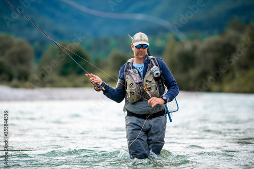 Fotografía Close up of a fly fisherman casts his line while wading in the middle of a river