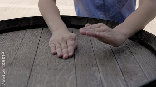 Children's hands knock on a wooden barrel. Sunny summer day. Close-up.