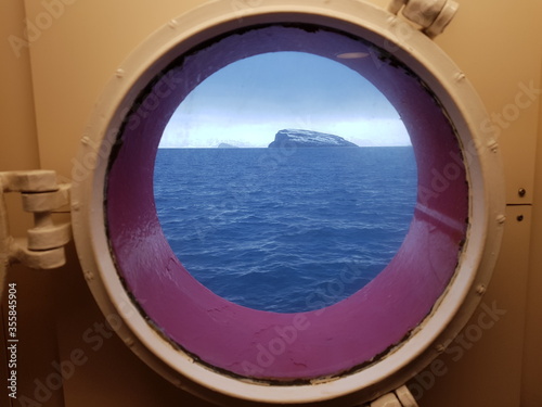 snowy mountain and waves on the arctic circle sea through a porthole