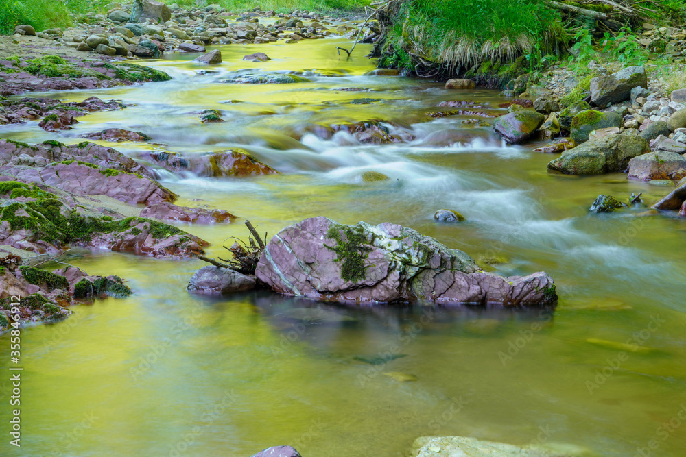 Long exposure picture of a stream flowing with rocks and natural light
