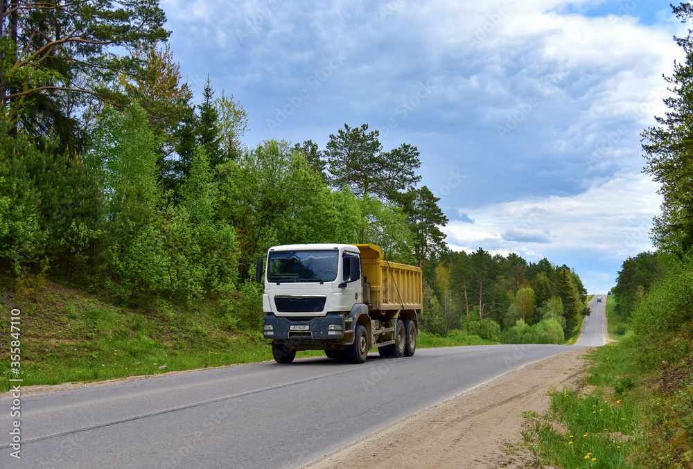 Tipper Dump Truck transported sand from the quarry on driving along highway. Modern Heavy Duty Dump Truck with unloads goods by itself through hydraulic or mechanical lifting