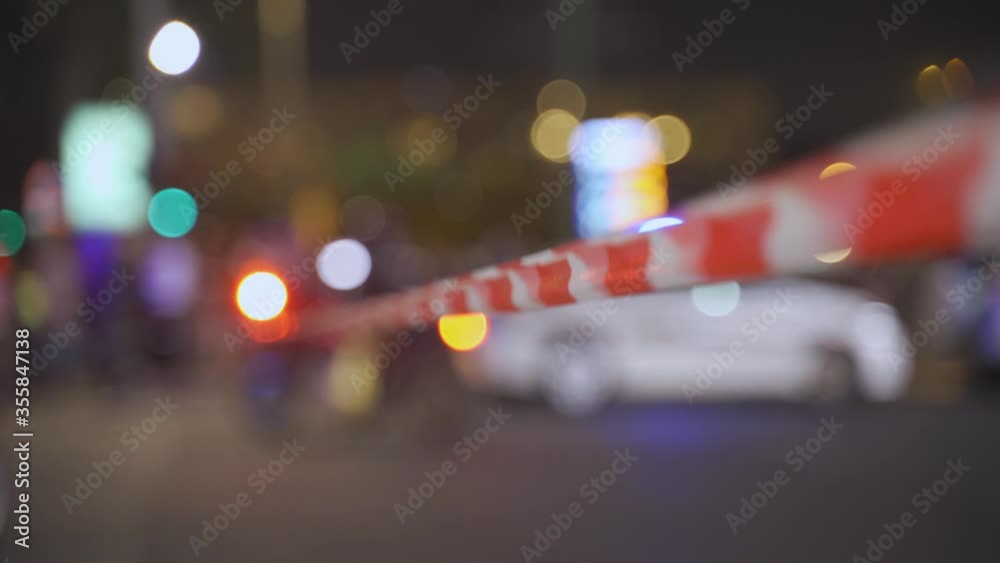 Police Red and White do not cross tape or ribbon with a police patrol car and sirens flashing in background Police Red and White do not cross tape or ribbon with a police patrol car and sirens flashing in background