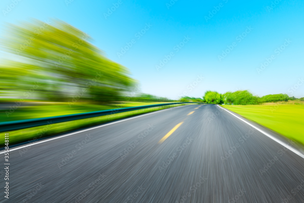 Fototapeta premium Motion blurred asphalt road and green tree landscape.