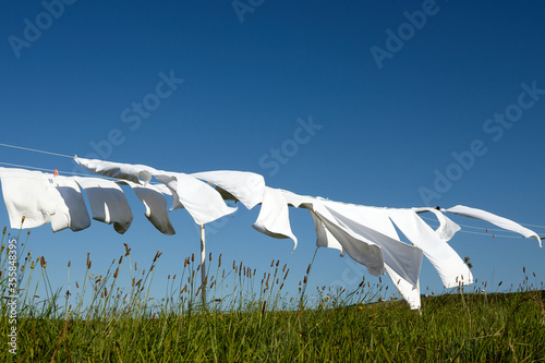 clean white clothes hanging on a rope moved by the wind in green meadow