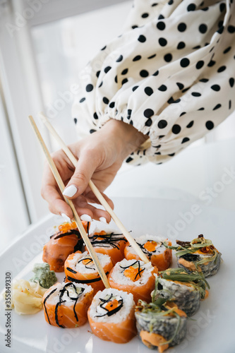 Rolls and sushi on a white plate. Hand with sushi sticks. 