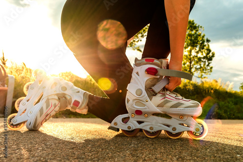 A woman tightens roller skates on the path. Woman's legs with roller blades at sunny day.