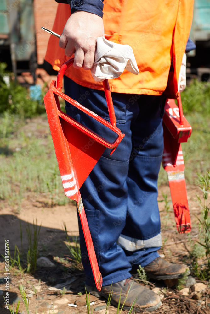 Fototapeta premium a railway worker in an orange signal vest and arms holds in his hand a red brake shoe