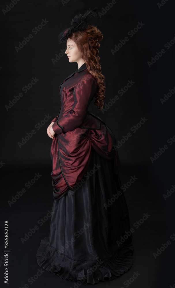 A young Victorian woman in a dark red and black ensemble against a black backdrop A young Victorian woman in a dark red and black ensemble against a black backdrop