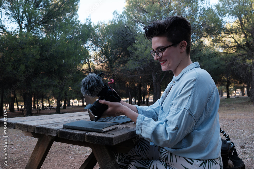 Young woman and creator is checking what she just recorded on her DSLR camera. She's Smiling.