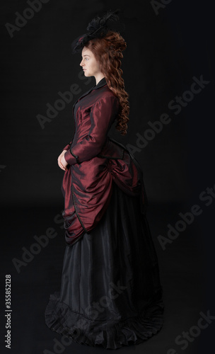 A young Victorian woman in a dark red and black ensemble against a black backdrop