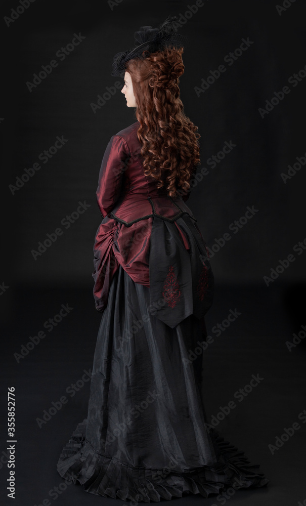A young Victorian woman in a dark red and black ensemble against a black backdrop