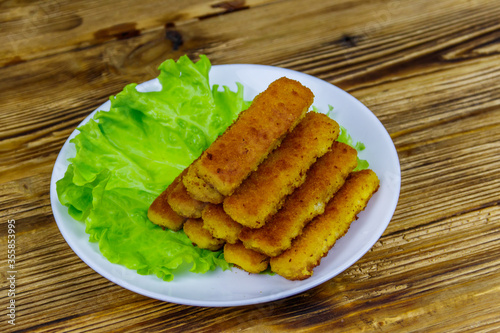 Fried fish fingers on a plate with lettuce on wooden table