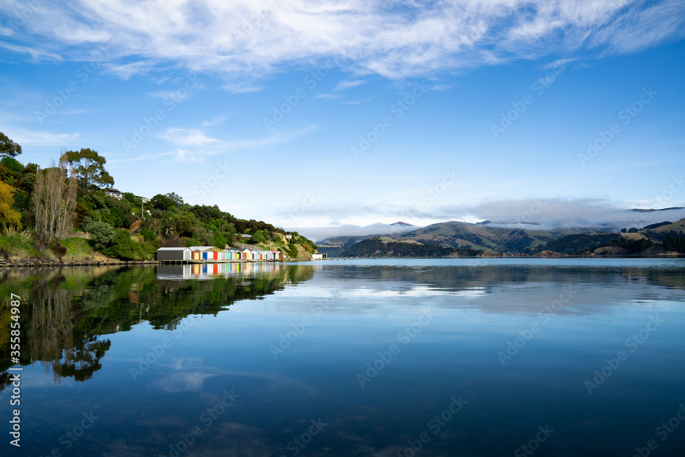 Colorful Boat Sheds with beautiful reflection on daytime  at Duvauchelle, Akaroa Harbour on Banks Peninsula in South Island, New Zealand.