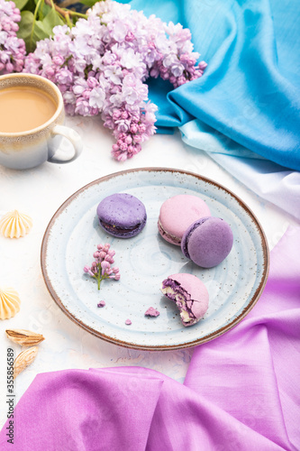 Purple macarons or macaroons cakes with cup of coffee on a white concrete background. Side view.