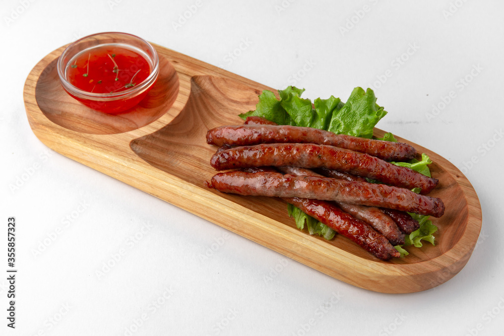 Hunting sausages with sauce on a wooden stand. Banquet festive dishes. Gourmet restaurant menu. White background. Hunting sausages with sauce on a wooden stand. Banquet festive dishes. Gourmet restaurant menu. White background.